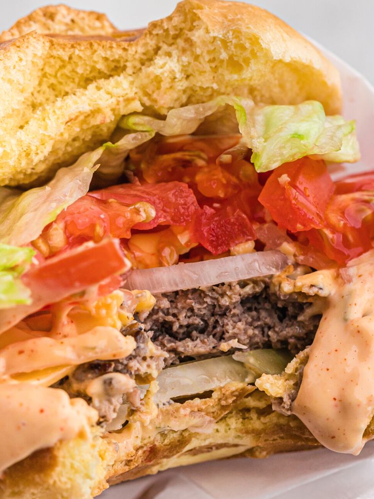 A close up bite shot of a burger with toppings, sauce, and a beef patty. 