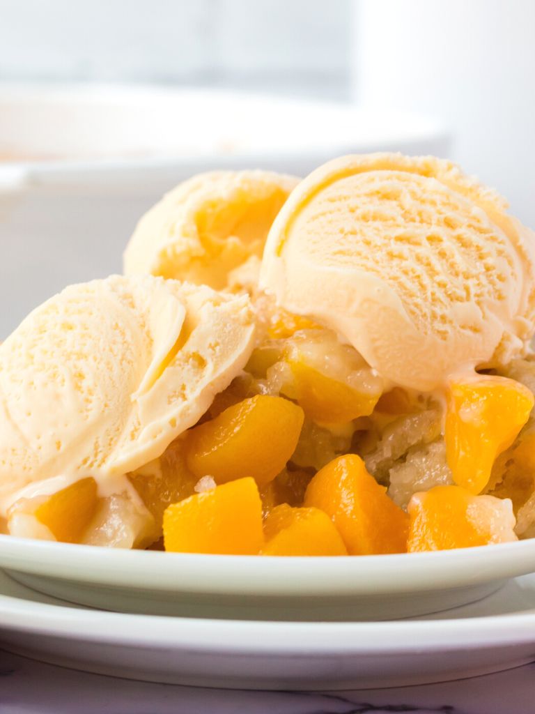 A plate with peach dessert on it and topped with ice cream.
