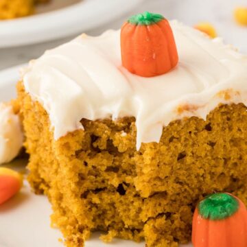 A slice of pumpkin cake with cream cheese frosting and decorated with a candy pumpkin.
