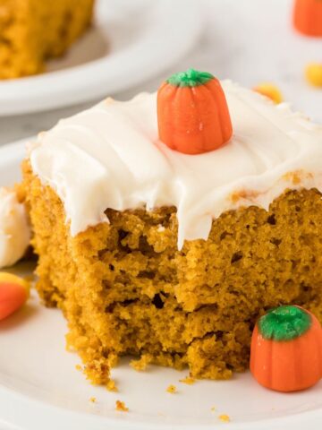 A slice of pumpkin cake with cream cheese frosting and decorated with a candy pumpkin.