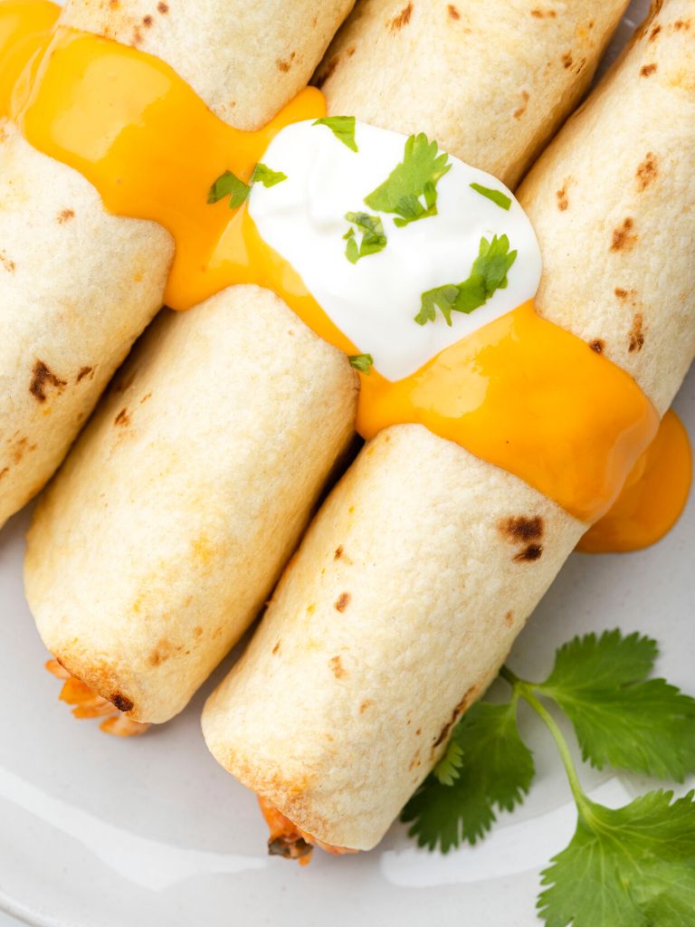 Overhead picture of flautas topped with nacho cheese sauce and sour cream.