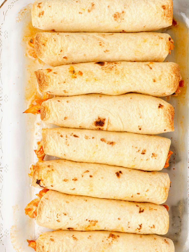 A dish with flour tortilla flautas inside of it that have been baked.
