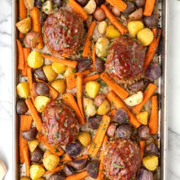 Overhead picture of a sheet pan with vegetables on it and mini meatloafs.