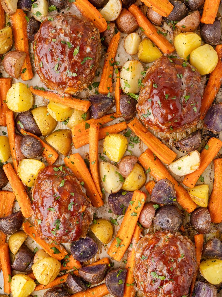 Close up shot of a sheet pan dinner recipe with carrots, potatoes, and ground beef meatloaf in mini shapes. 