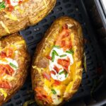 Air fryer basket filled with prepared, cooked baked potatoes inside of it.