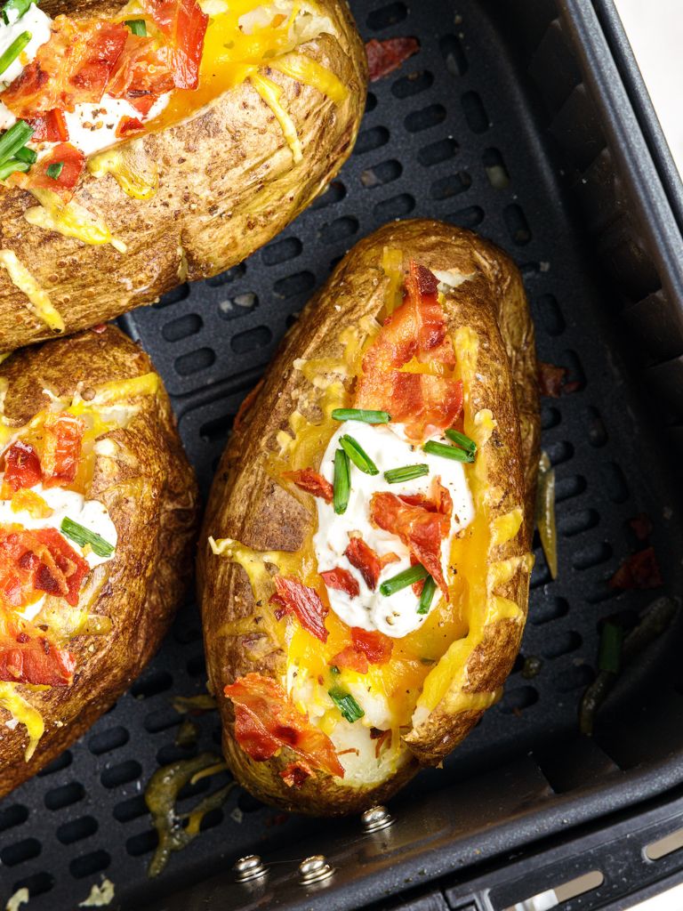 Air fryer basket filled with prepared, cooked baked potatoes inside of it. 