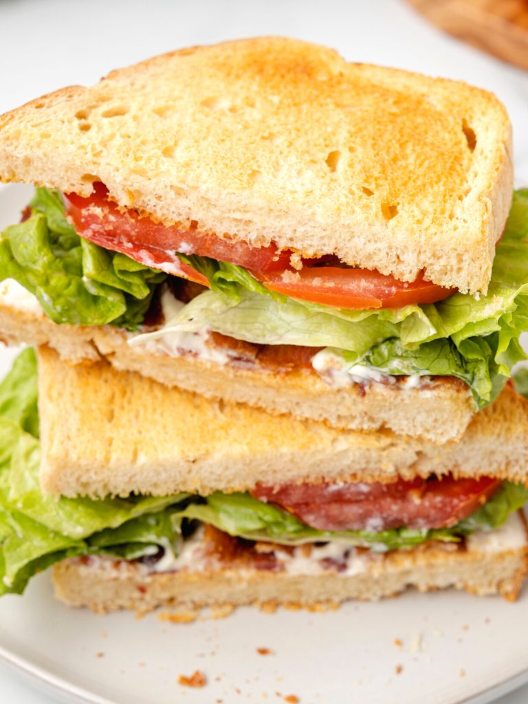 Stack of sandwiched with bacon, lettuce, and tomato on a white plate. 