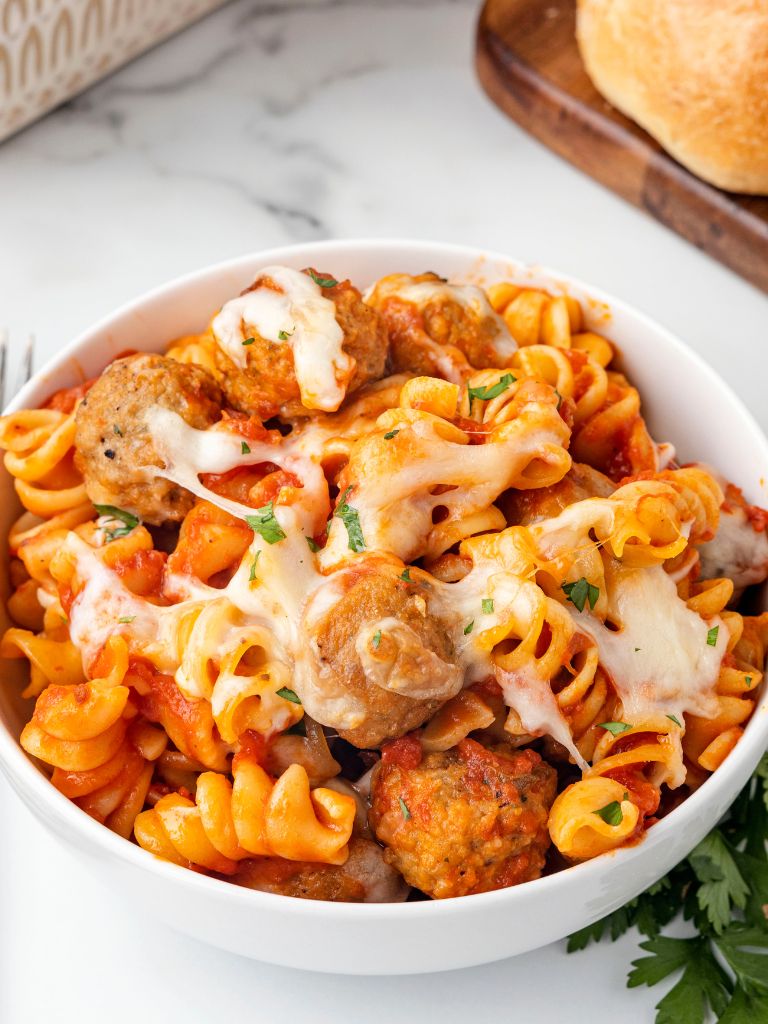 A bowl of pasta, meatballs, and cheese.