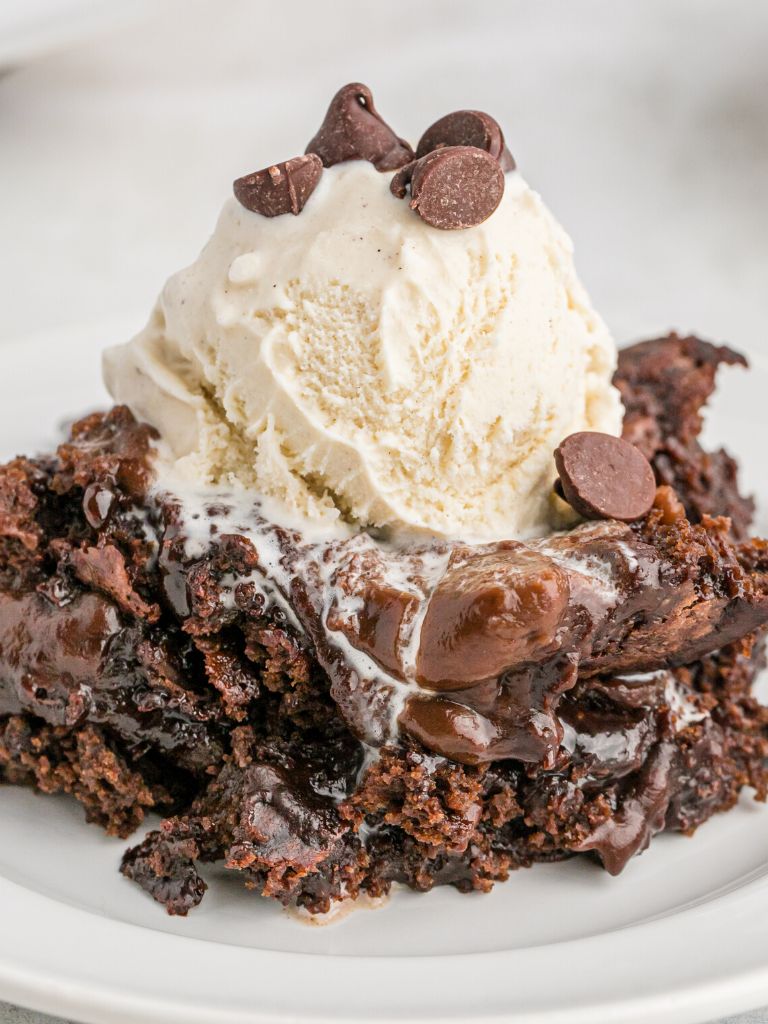 A serving of fudge cake on a white plate with a scoop of ice cream that is melting into the warm cake. 