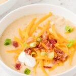 A white bowl with soup inside of it topped with cheese, bacon, and sour cream.