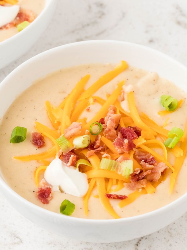 A white bowl with soup inside of it topped with cheese, bacon, and sour cream. 