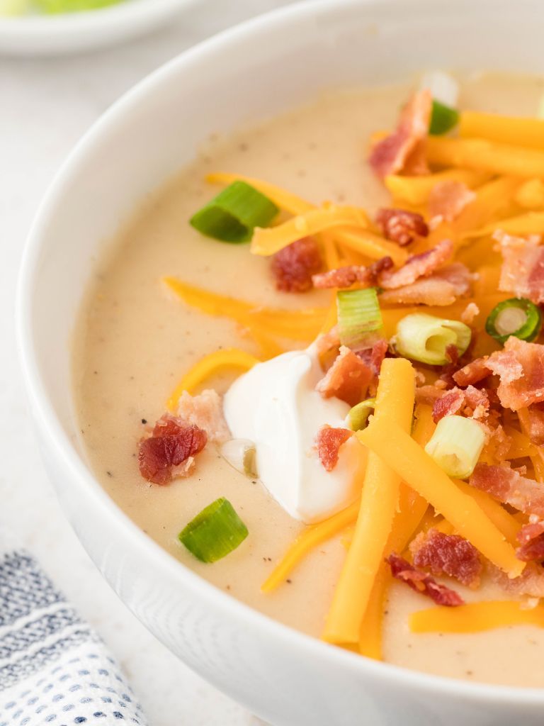 Overhead picture of potato soup that is made with mashed potatoes. The bowl of soup is topped with bacon, cheese, sour cream, and green onions.