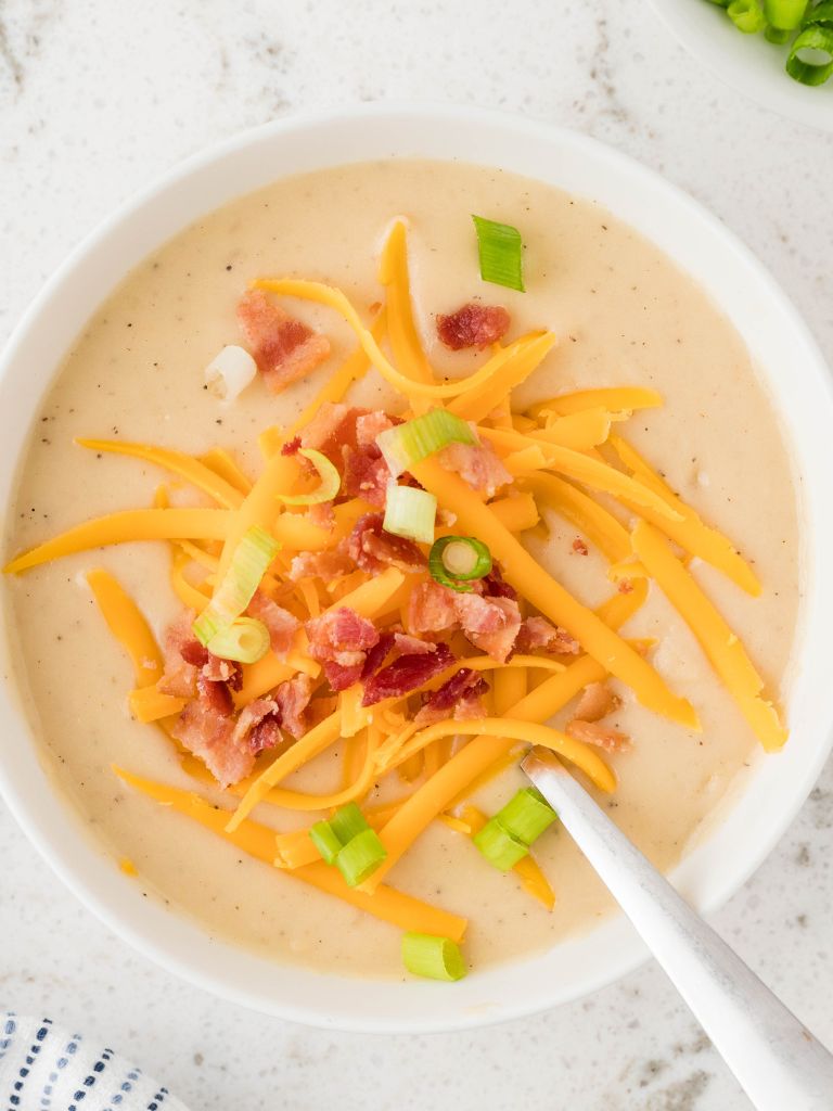 Overhead photo of a bowl of soup with a spoon inside the soup and topped with garnishes. 