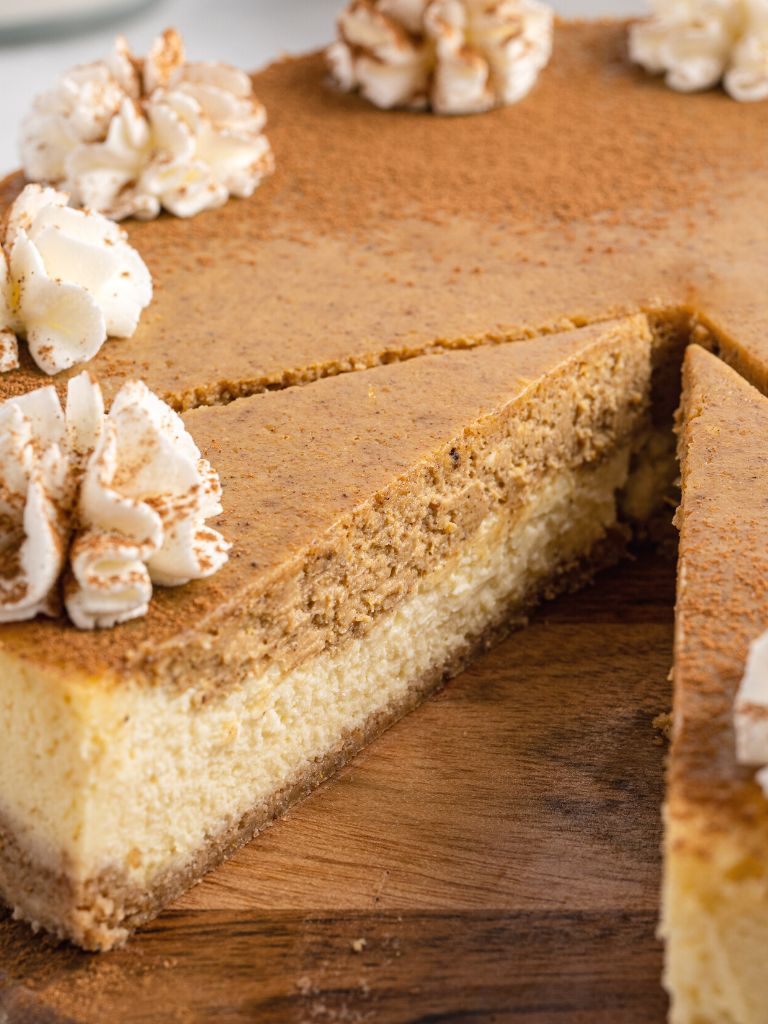 A side view of a slice of cheesecake with pumpkin layers on top of a wooden board.