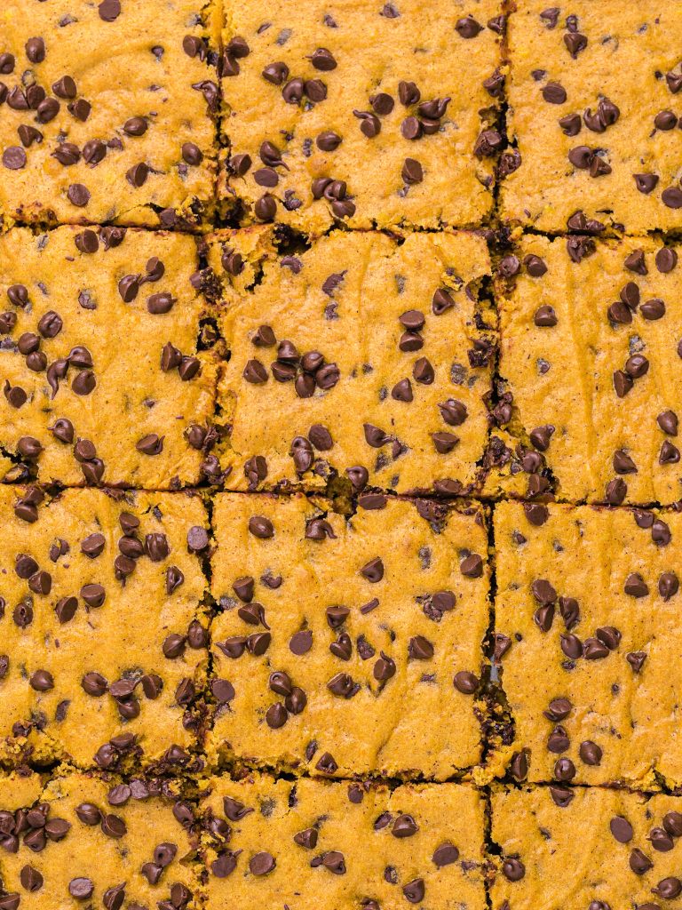 Overhead picture of a cookie sheet with a pumpkin bar recipe inside in and topped with mini sized chocolate chips.