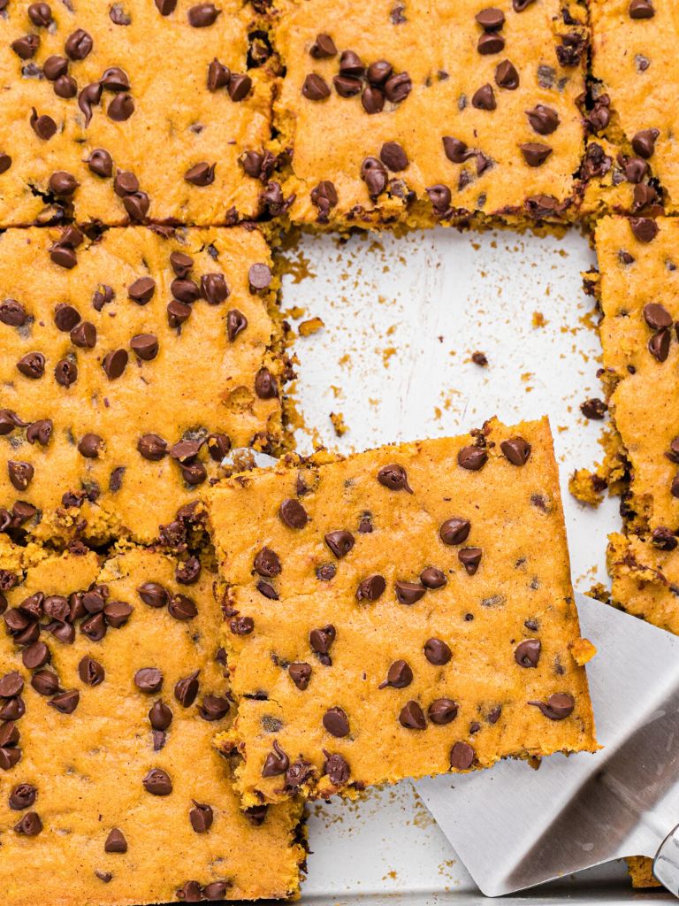 A pan of pumpkin bars with a silver spatula holding a square on it. 