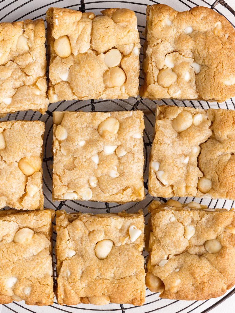 Overhead shot of cookie bars on a wire rack with white chocolate chips and macadamia nuts. 