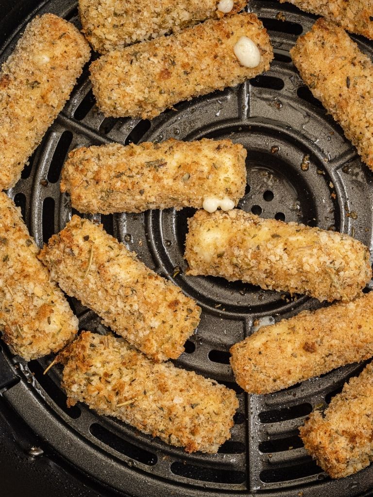 An air fryer basket filled with cooked mozzarella sticks in it. 