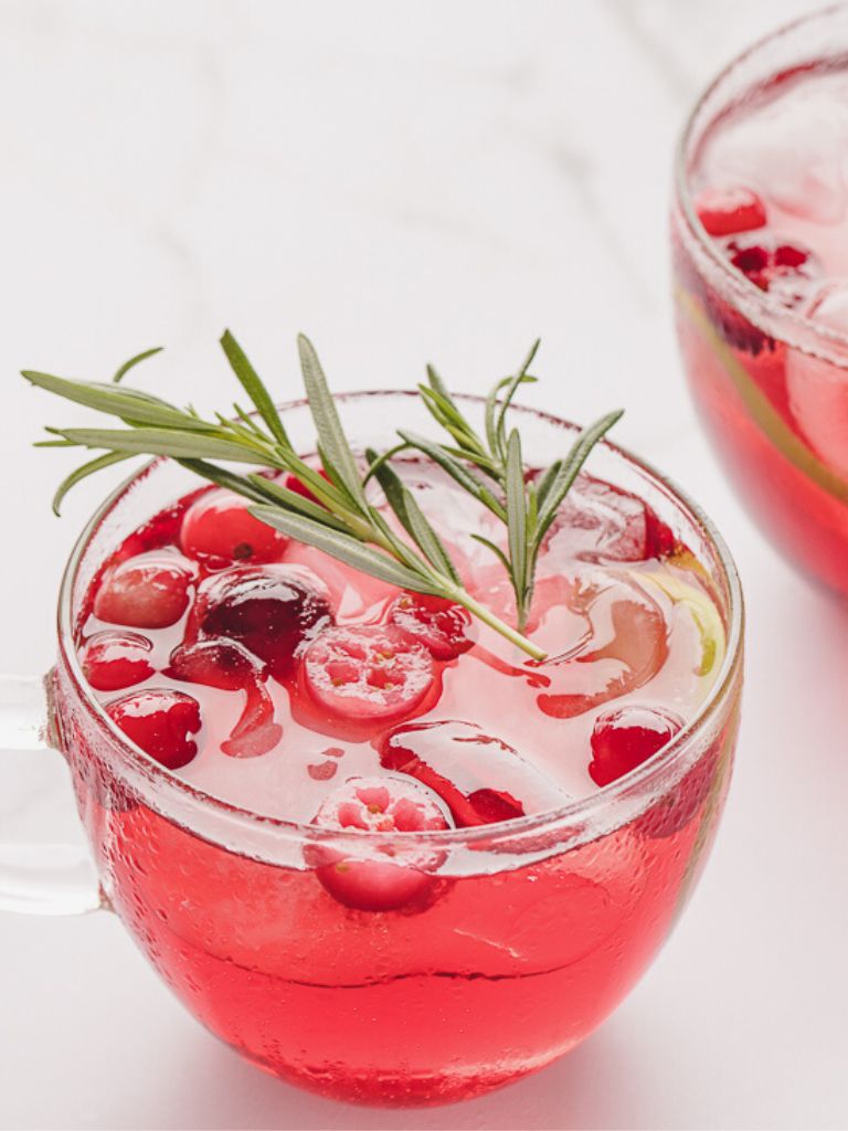 A glass cup of punch garnished with a rosemary twig. 