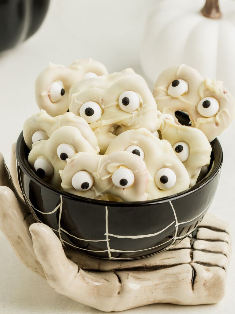 A black bowl of pretzel ghosts with eyeballs.