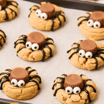 Tray of cookies topped with spiders sitting on a baking sheet.