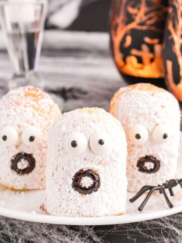 Twinkie ghosts sitting on a white plate with halloween decor in the background.