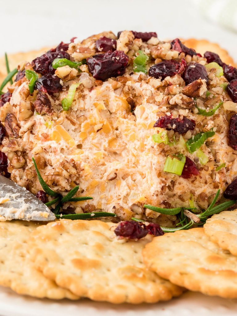 A cheeseball covered in dried cranberries and pecans with rosemary sprigs on it. 