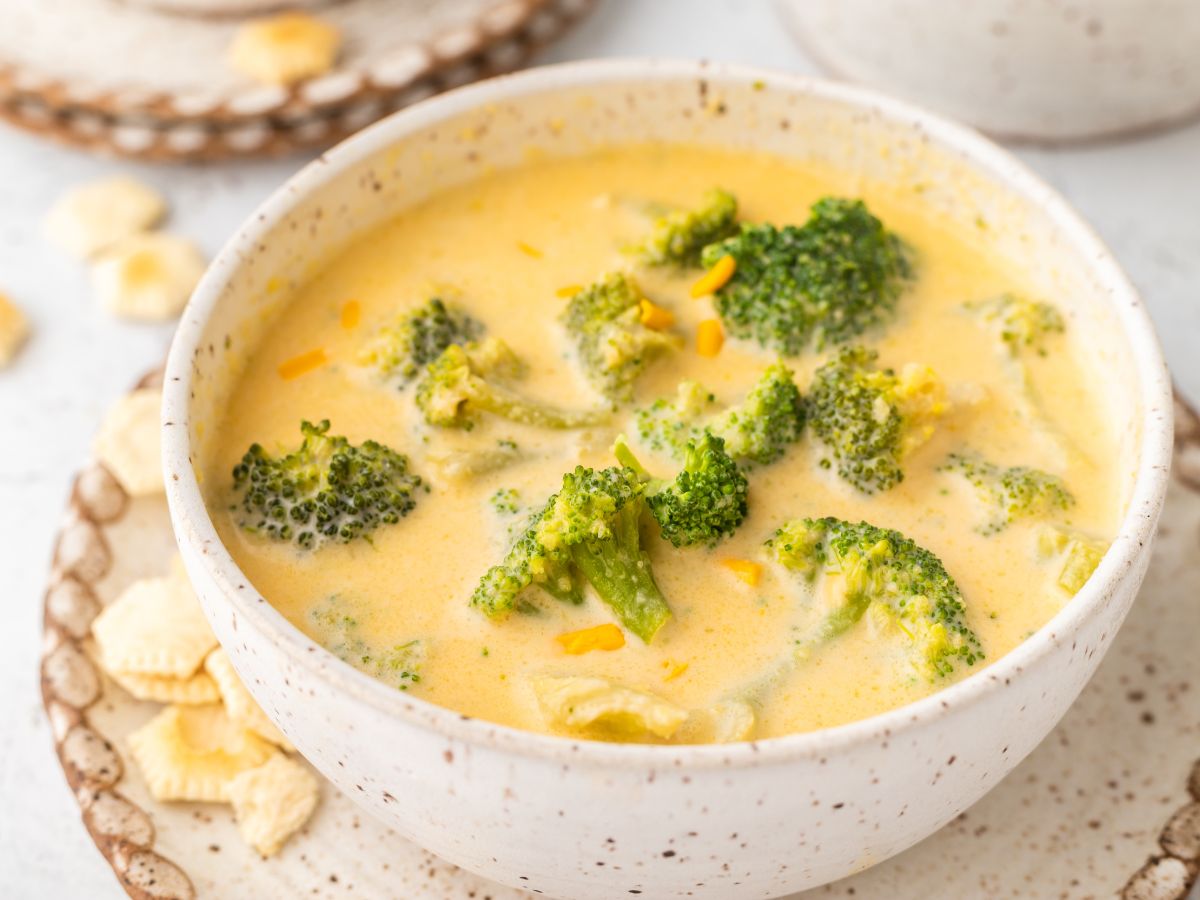 Soup inside a bowl with broccoli and crackers to the side of it. 