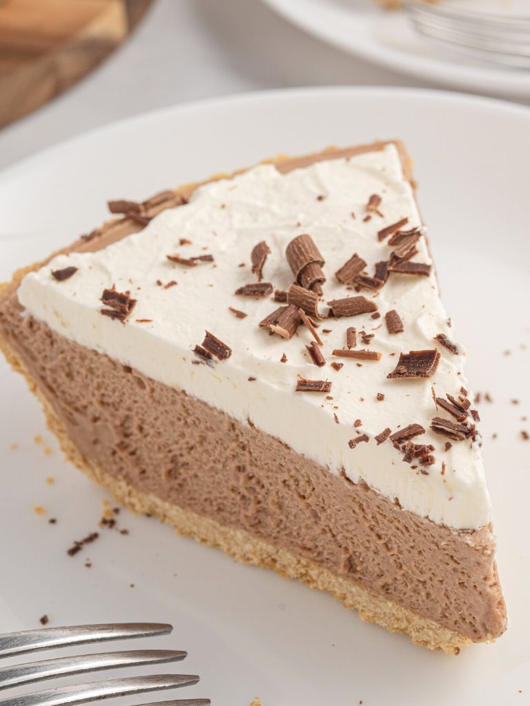 A slice of pie with a white plate and chocolate curls on top of it. 