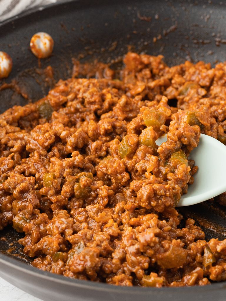 A skillet pan of sloppy Joe meat with a spoon inside the mix. 