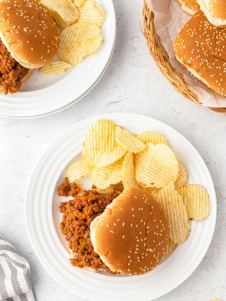 Overhead shot of dinner plates with a bun of sloppy Joe meat and chips to the side of each plate. 