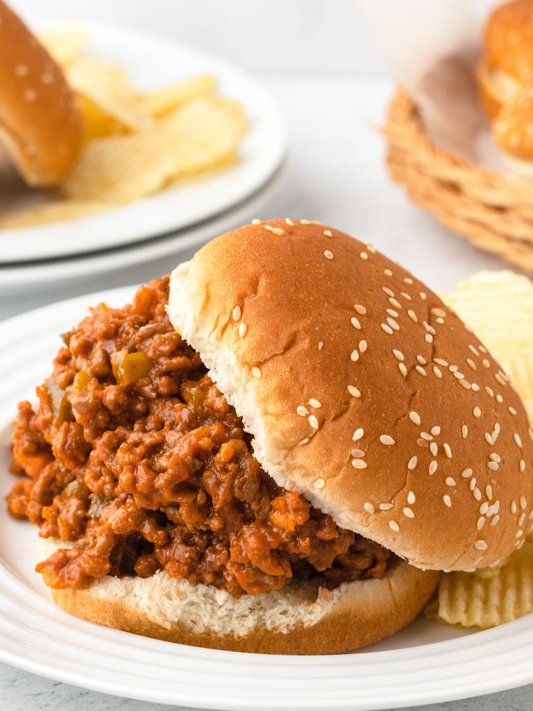 White plate with a sloppy Joe on it and chips to the side of it. 