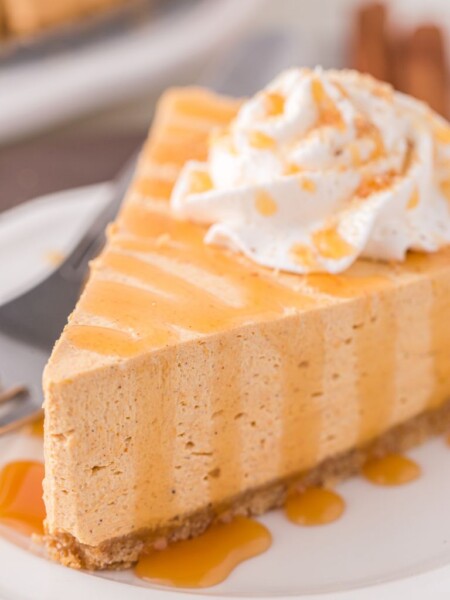 A slice of cheesecake on a white plate with caramel sauce drizzled over top of it.