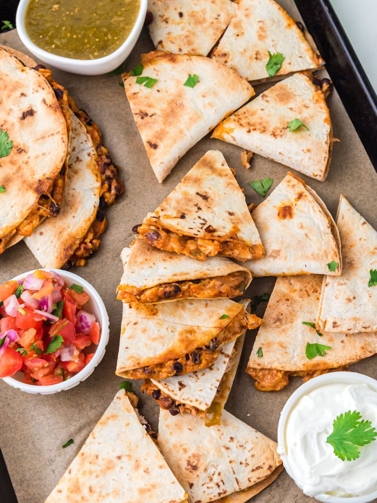 Sheet pan of chicken quesadillas stacked and bowls of dipping sauce to the side. 