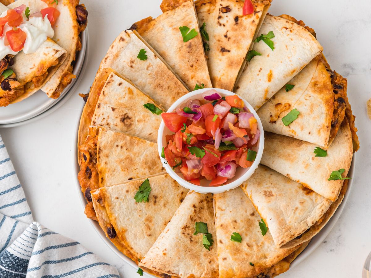 Plate of quesadillas with flour tortillas and a bowl of salsa in the center of them all. 