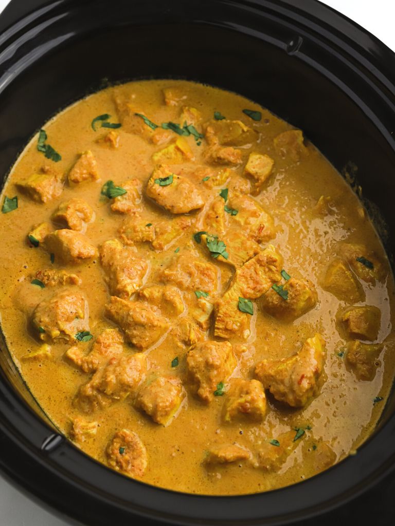 View of a slow cooker with chicken and butter sauce inside of it. 