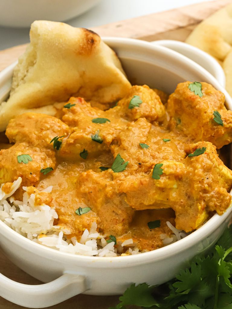 A bowl of butter chicken over rice and a side of naan bread inside the bowl. 