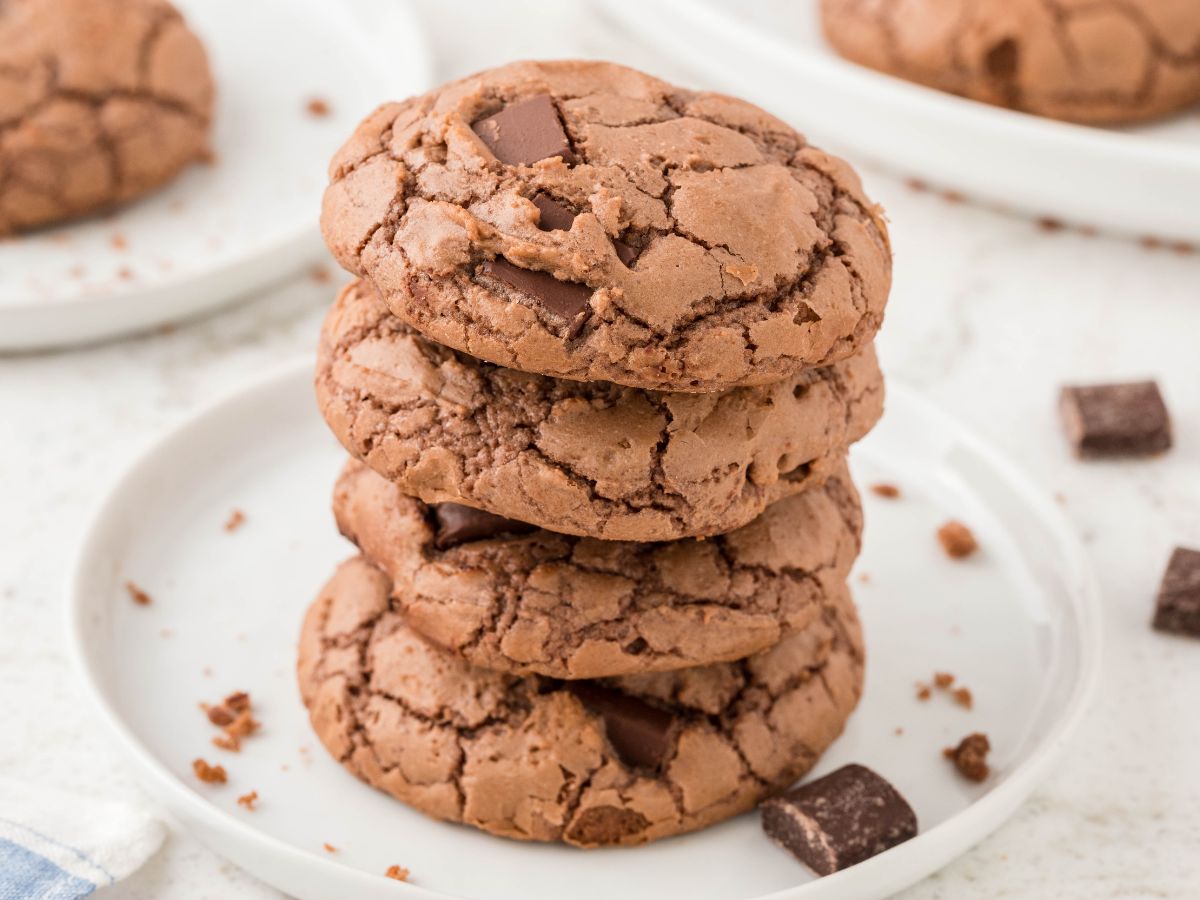Stack of cookies on a white plate with chocolate chunks around it. 