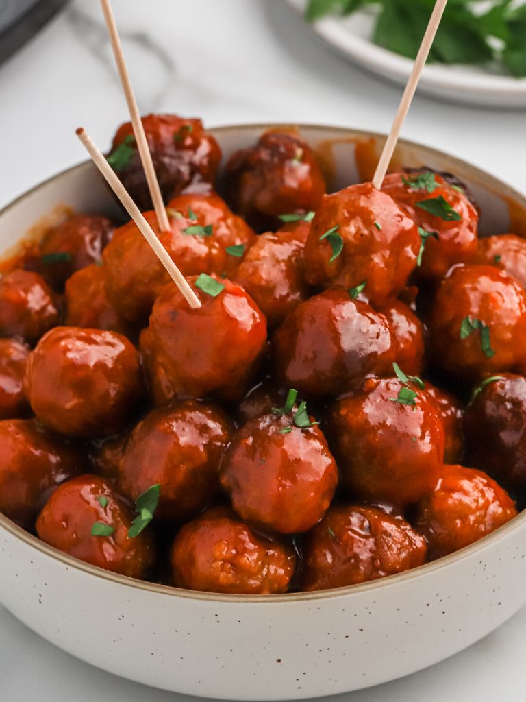A bowl of meatballs and sauce with toothpicks in the meatballs. 
