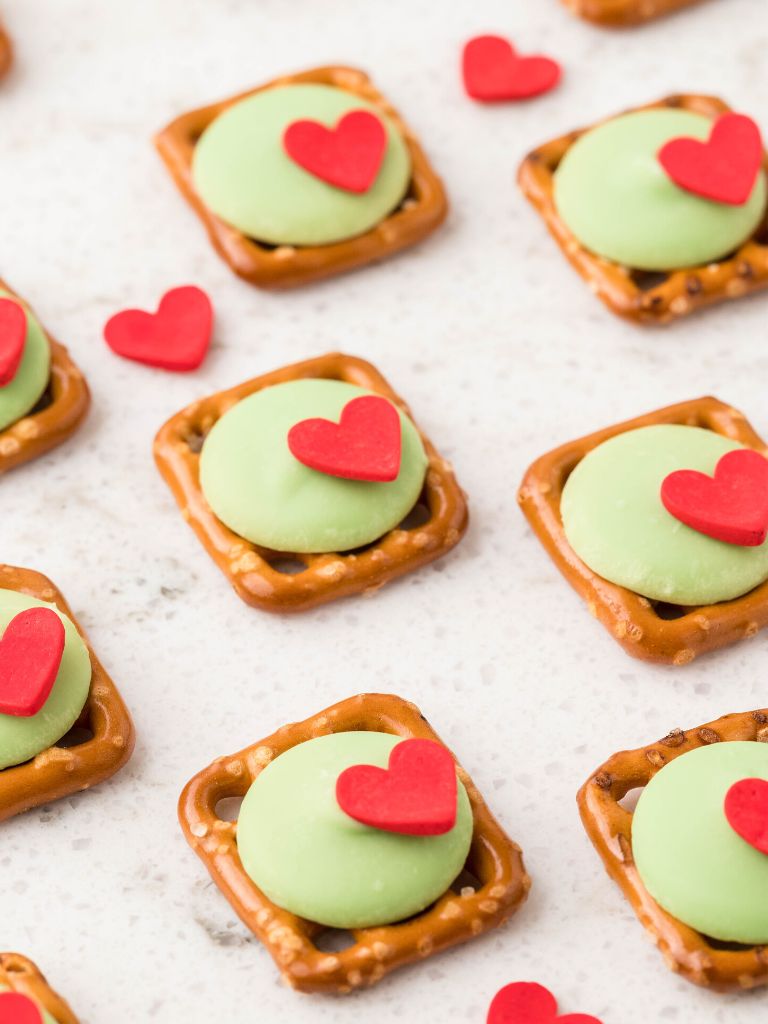 Evenly spaced pretzel bites with a green candy melt on them and a red heart for decoration. 