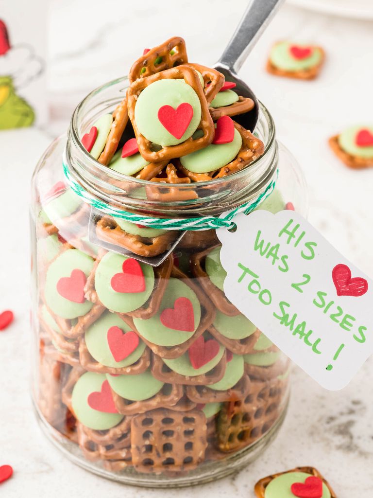 Grinch pretzels inside a glass jar with a note on the side of it. 