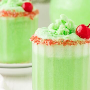 A cup of green grinch punch topped with a sugar rim and cherry.