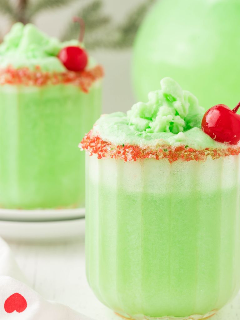 A cup of green grinch punch topped with a sugar rim and cherry. 