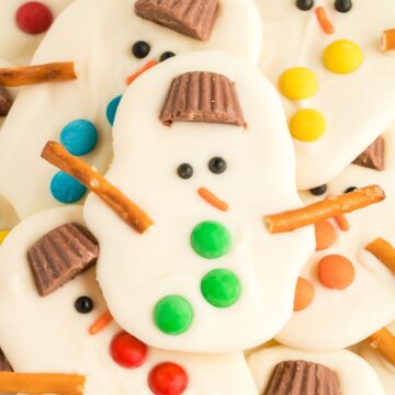 Close up of a snowman bark recipe with a hat, button, and pretzels sticks for the arms.