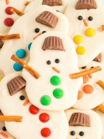 Close up of a snowman bark recipe with a hat, button, and pretzels sticks for the arms.