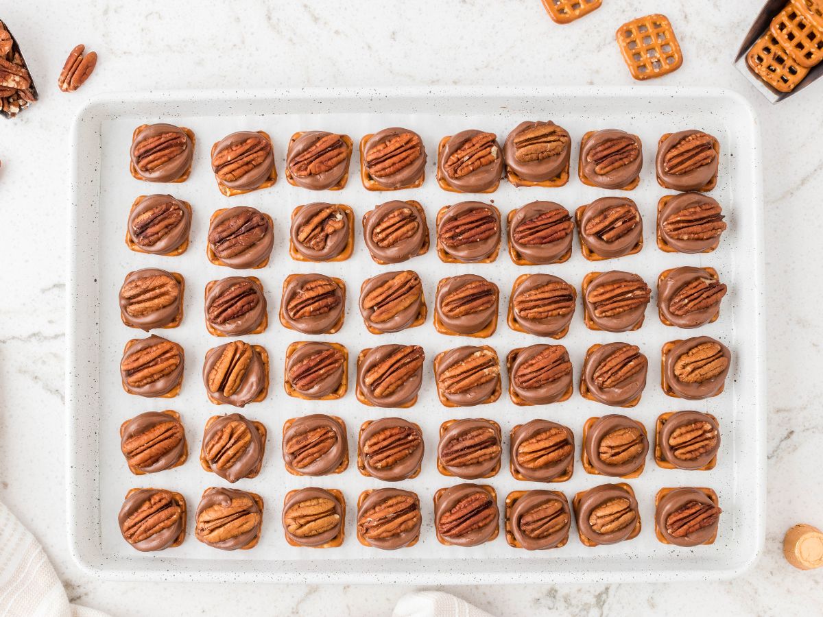 Horizontal image of rows of turtle pretzels on a cookie sheet. 