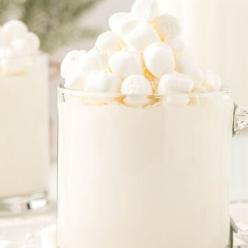 A glass mug of hot chocolate that is white from white chocolate chips. Topped with mini marshmallows.