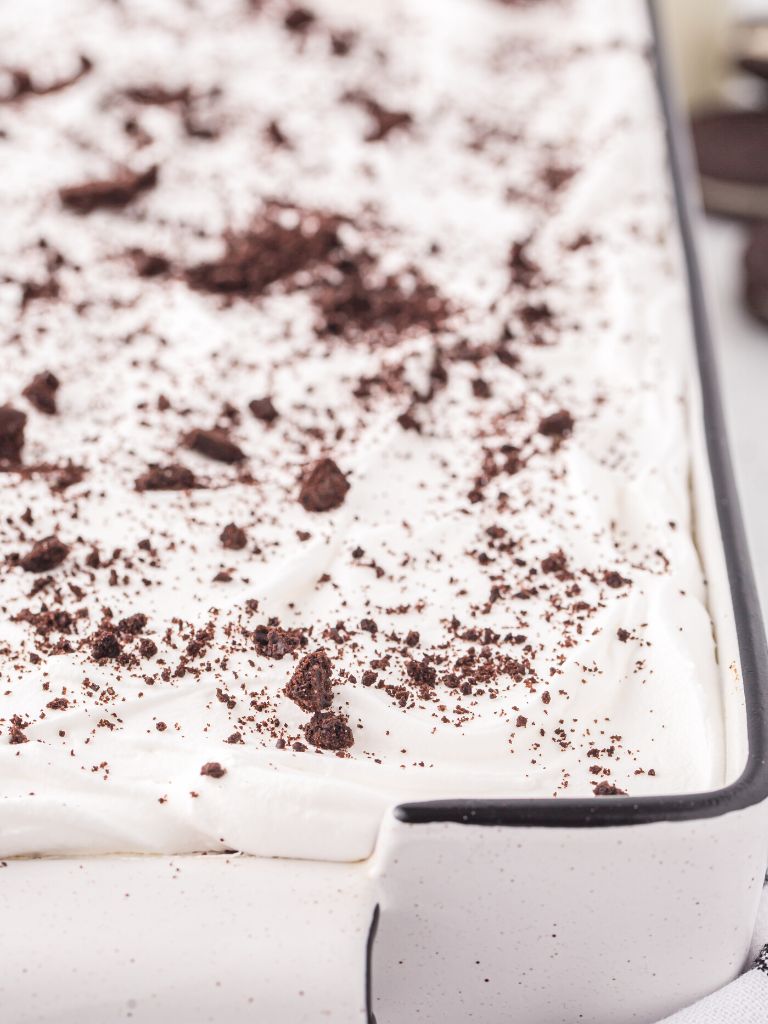 A cake topped with cool whip and chopped oreo crumbs. 