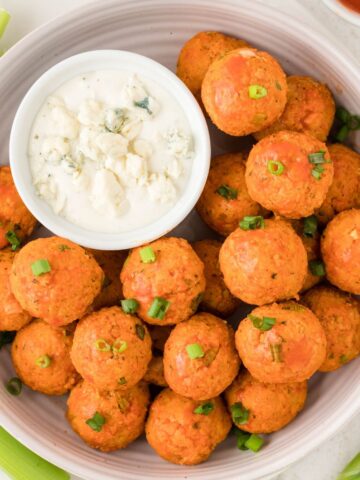 A white serving bowl of meatballs with a bowl of ranch sauce to the side.