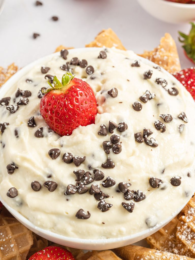 A sweet dip with mini chocolate chips on top, a strawberry, and dusted with p[powdered sugar.